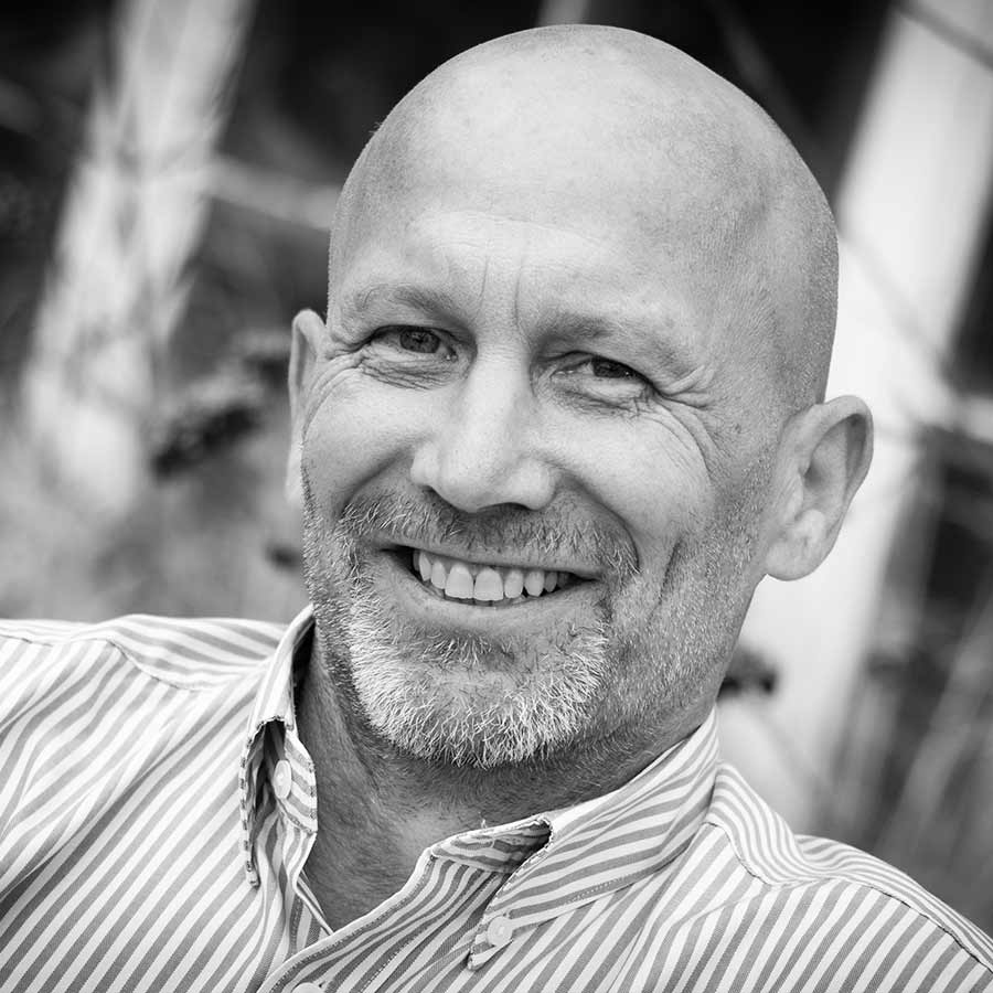 Black and white photo of a bald male in stripey shirt smiling and looking into the camera