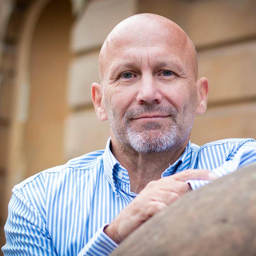 Bald male in stripey shirt, leaning on a sculpture and looking into the distance