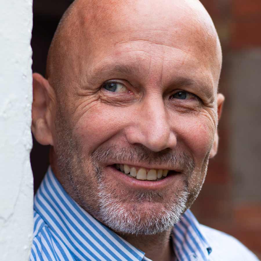 Bald male in stripey shirt smiling and looking into the distance