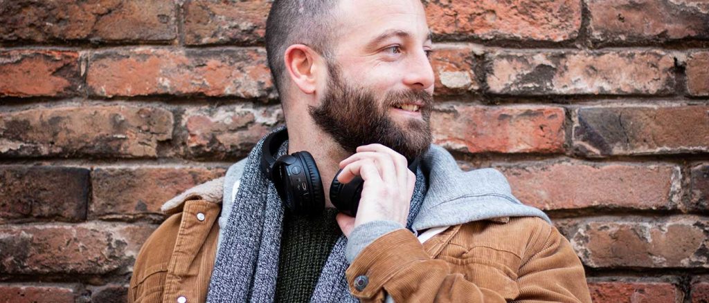 Dating client with headphones around his neck in front of a brick wall