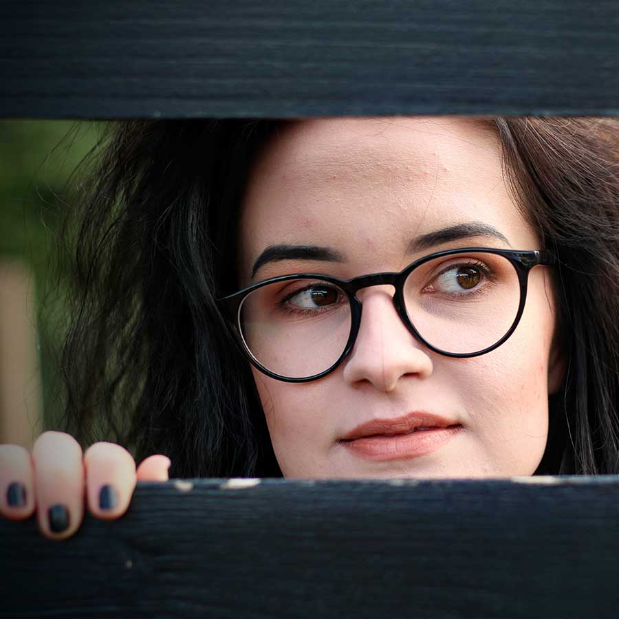 Female with dark hair and black rimmed glasses peeking through a gap