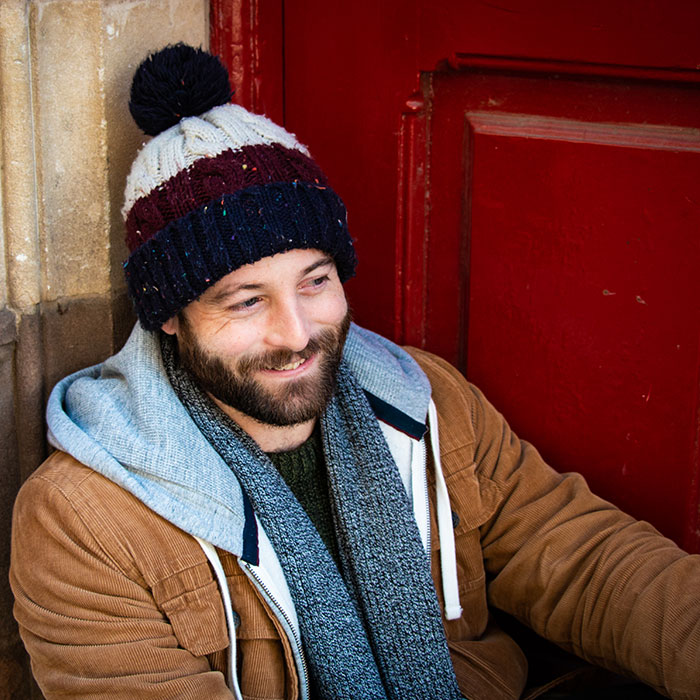 Dating photo of a male in a woolly hat sat in a red doorway