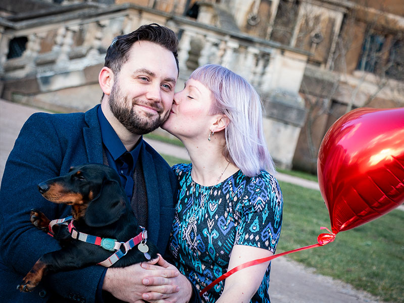 A couple holding their dog and a red love heart balloon