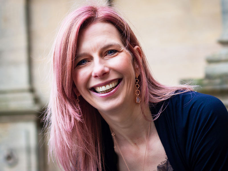 A woman with pink hair looking and smiling into the camera