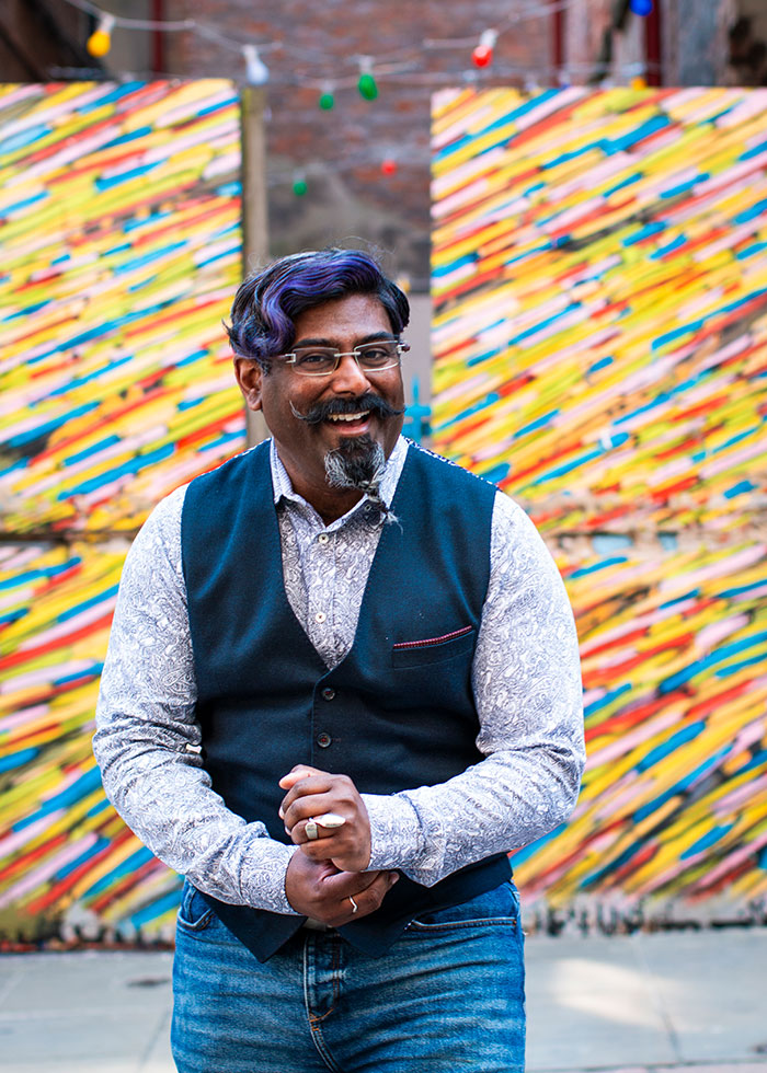 Online dating photo of male fastening his sleeve buttons. He stands in front of a multicoloured gate. Captured by Dating Profile Photographer, Gemma Wilks | We Just Clicked