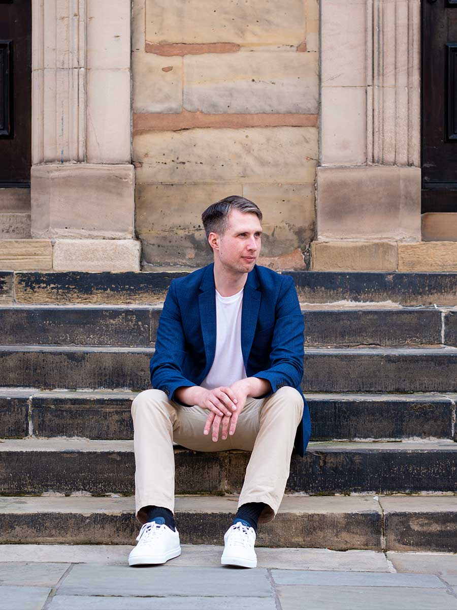 Male sat on stone steps in beige chinos, white t-shirt, ad blue blazer as part of his dating profile revamp experience