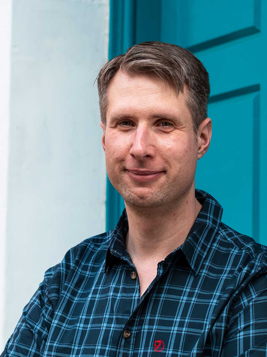 Male leaning against a bright blue door, smiling into the camera.