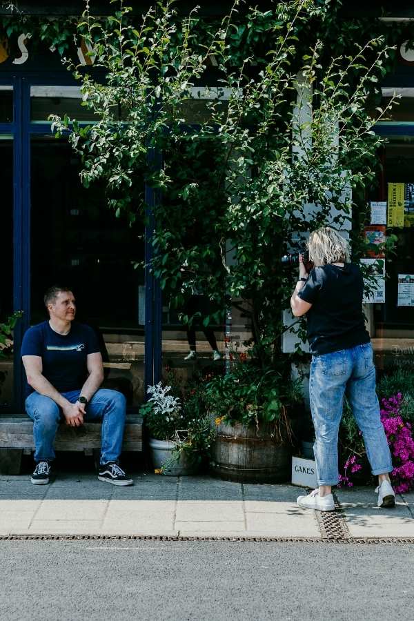 Dating Profile Photographer, Gemma, taking photos of a guy sat on a bench, surrounded by foliage.